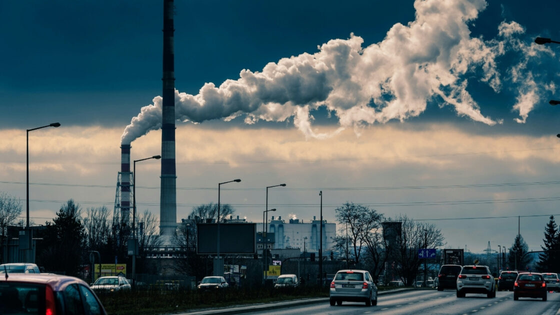 Imagem de fumaça saindo da chaminé de fábricas e indo em direção à cidade. Em primeiro plano, vêem-se carros circulando. A tecnologia desenvolvida pela GLR Tech filtra CO₂ e poluentes do ar. 