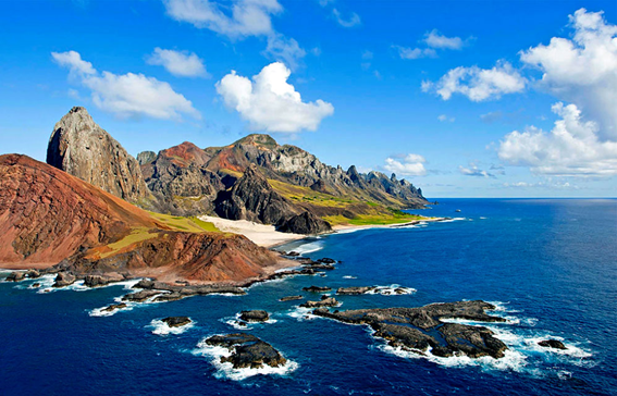 Descrição alternativa: Imagem da Ilha da Trindade, isolada no oceano, rodeada pelas águas azul-escuras da Amazônia Azul. A paisagem destaca formações rochosas, vegetação nativa e a imensidão marinha que protege uma biodiversidade única e ainda pouco explorada.