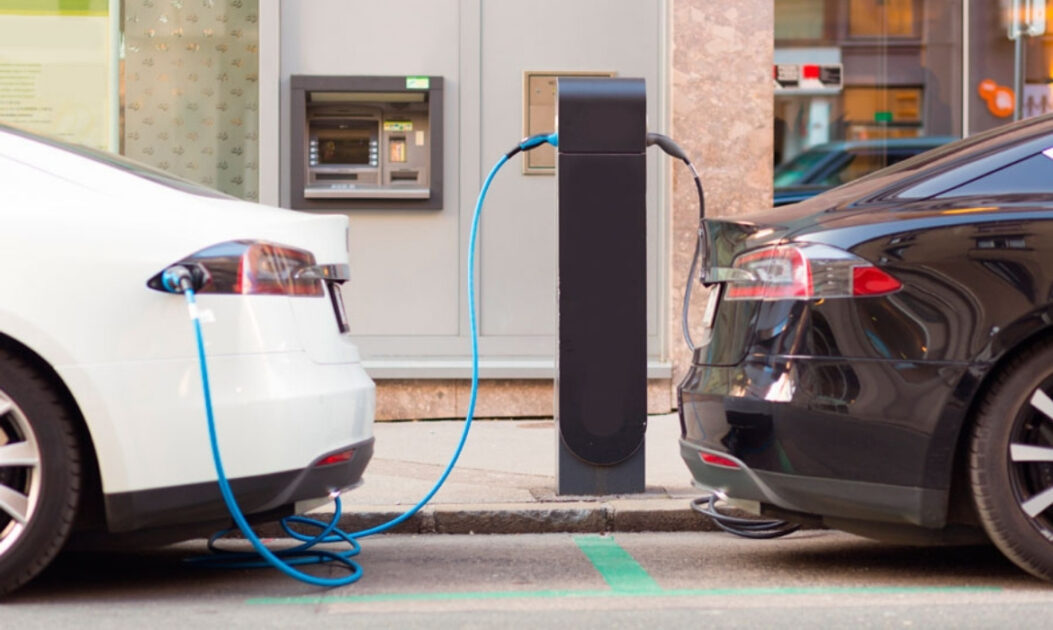 Carros elétricos conectados a estação de recarga em área urbana. 