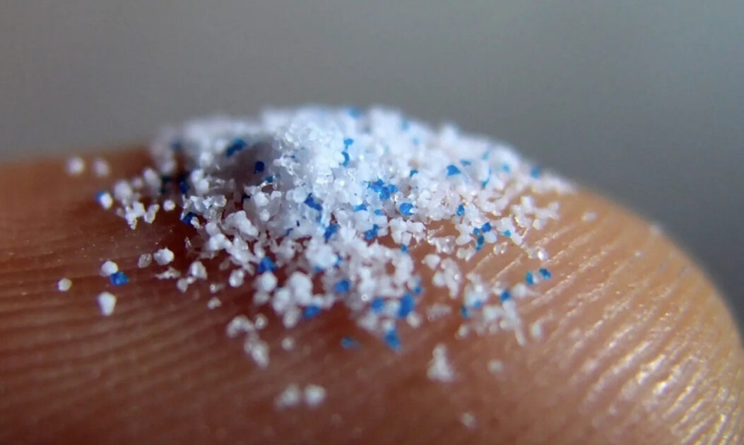 Partículas de microplásticos sobre o dedo humano, representando aditivos usados em produtos cosméticos como esfoliantes. Presença de partículas acende debate sobre perigos dos nanoplásticos.