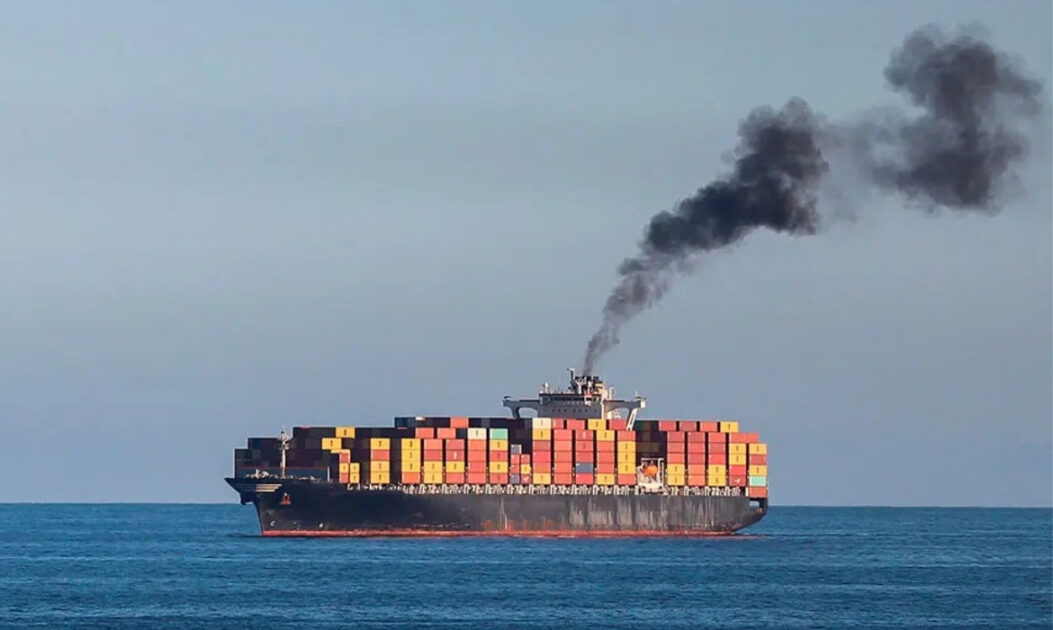 Navio cargueiro no oceano com chaminé emitindo fumaça escura, ilustrando o impacto climático do transporte marítimo e a necessidade da descarbonização marítima.