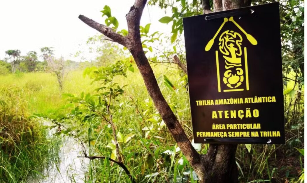 Placa oficial da Trilha Amazônia Atlântica instalada em área de vegetação no Pará.