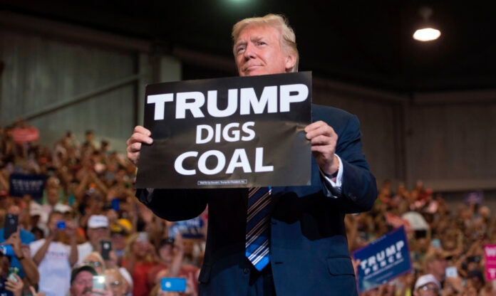 Donald Trump sorrindo e segurando uma placa com os dizeres “Trump Digs Coal”, em referência ao apoio ao setor de combustíveis fósseis.