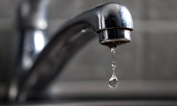 Torneira com vazamento desperdiçando água tratada em área urbana.