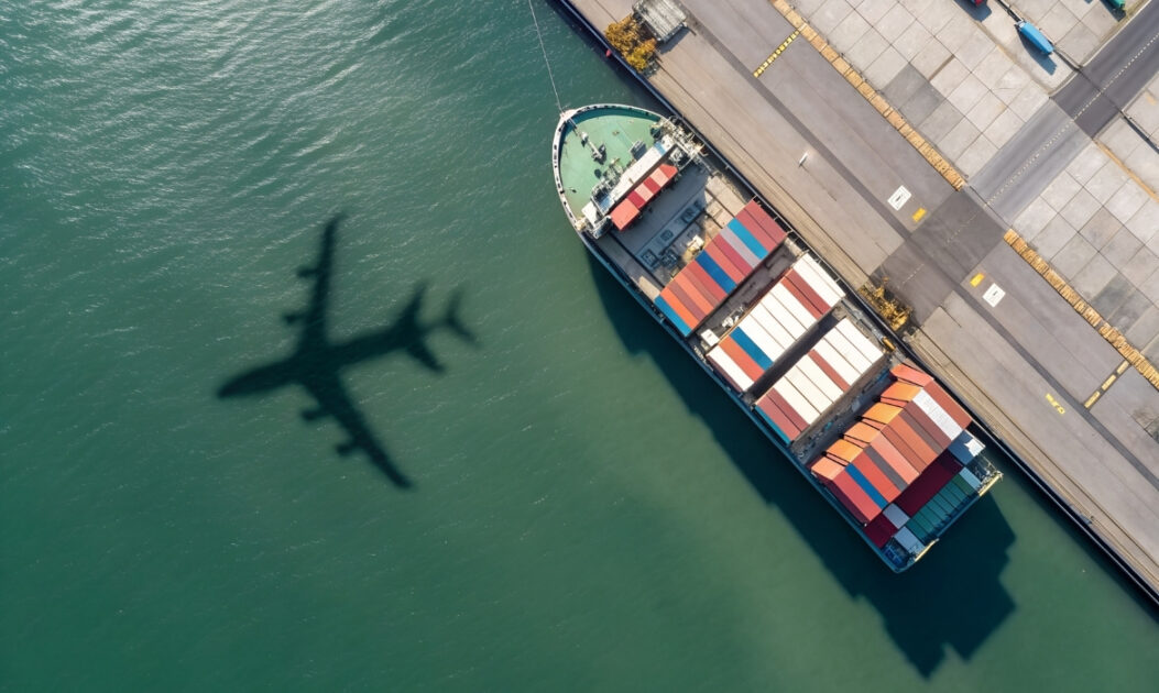 Sombra de um avião projetada sobre o mar ao lado de um navio cargueiro atracado, ilustrando setores que podem se beneficiar do uso de combustíveis sintéticos produzidos pela transformação do CO₂.