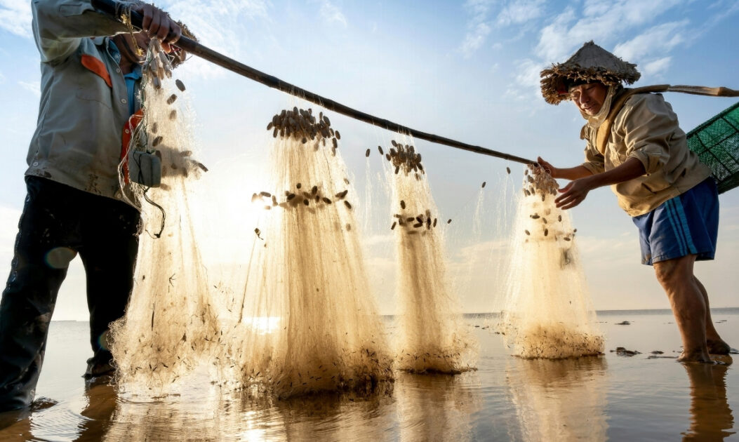 Pescadores carregam rede em local costeiro, representando modos de vida conectados aos oceanos — foco do Pacote Azul da COP30.