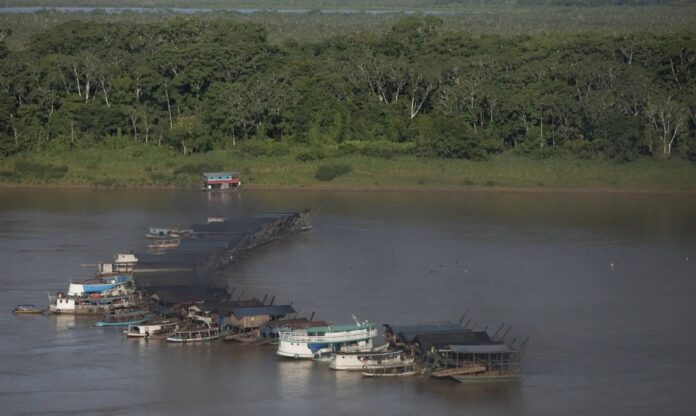 Vista aérea de comunidades ribeirinhas às margens de um rio amazônico, cercadas por floresta densa. Comunidades ribeirinhas vivem próximas aos rios amazônicos, onde a contaminação por mercúrio avança com o garimpo ilegal.