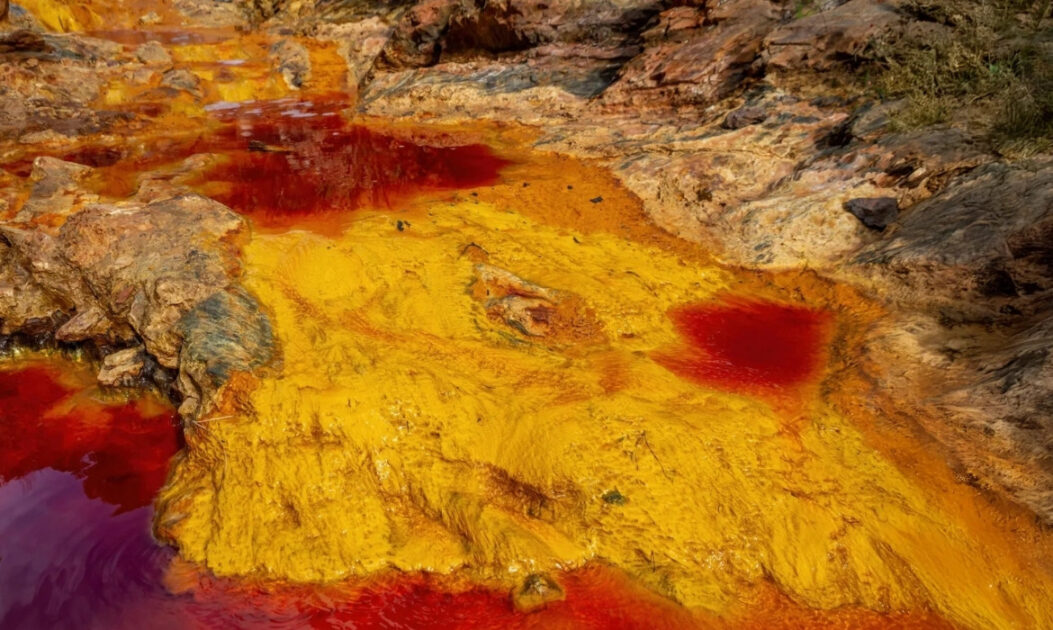 Bactérias que “respiram ferrugem” revelam novo metabolismo com impacto no clima global 1 Rio com coloração avermelhada causada pela oxidação de ferro, processo semelhante ao utilizado pelas bactérias MISO para gerar energia.