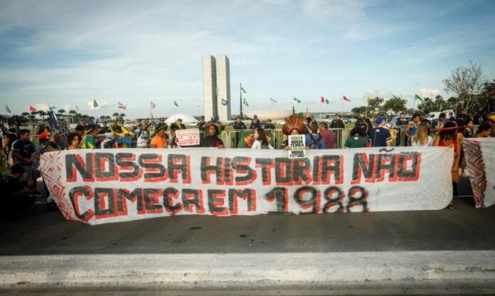 Indígenas com cocares e faixas protestam contra o marco temporal em frente ao Congresso Nacional.