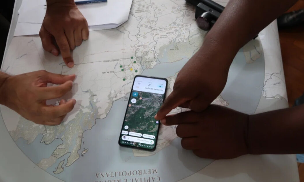 Mãos apontando para mapas em papel e em celular durante oficina de mapeamento de territórios quilombolas. 