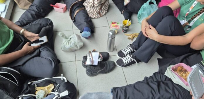 Funcionários da limpeza sentados no chão, próximos aos banheiros da Blue Zone da COP30, comendo sem estrutura adequada.