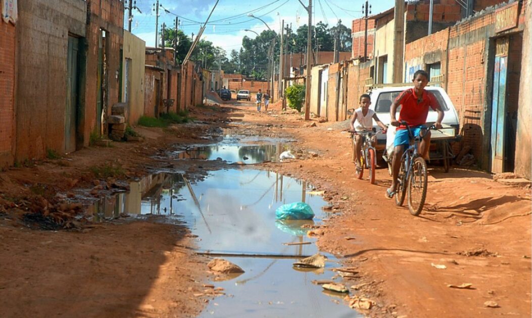 Crianças brincando em rua com água escorrendo, muitas comunidades continuam sem acesso à água tratada.