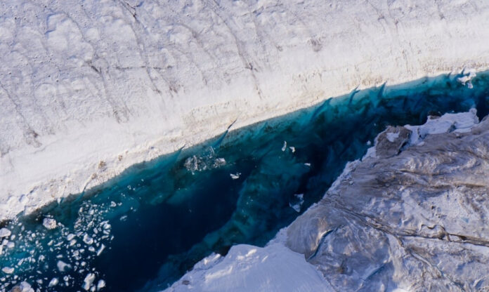Vista aérea de um lago formado sobre a geleira da Groenlândia, com rachaduras no gelo ao redor.