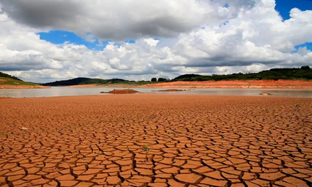 Vista aérea do Sistema Cantareira com níveis de água drasticamente baixos, evidenciando as marcas da seca e a exposição do solo rachado ao redor do reservatório.