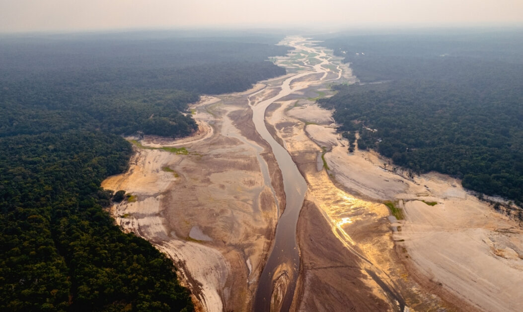 Paisagem da Amazônia afetada por secas quentes, com solo exposto, vegetação ressecada e árvores sob estresse hídrico causado pelo aumento das temperaturas.

A Amazônia já paga caro pela distância, pela dependência hidroviária e pela instabilidade histórica de investimentos estruturantes. Agora, paga também pela volatilidade climática. Ignorar essa soma é condenar a região à desvantagem permanente.