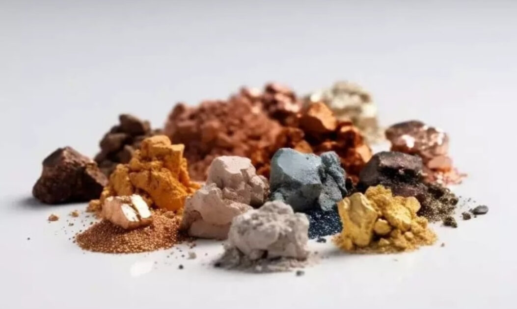 Fragmentos de minerais de terras raras extraídos, expostos em superfície escura, representando a base física da cadeia de suprimentos da inteligência artificial.