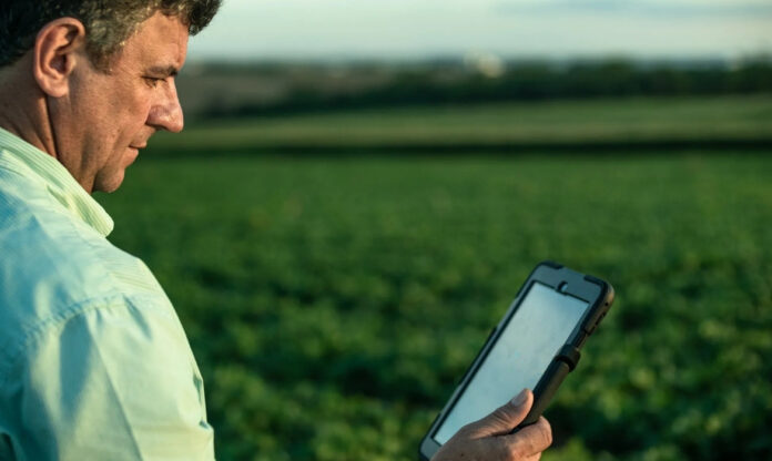 Agricultor segurando tablet em plantação ao fundo utilizando tecnologia da agricultura 4.0 no Brasil