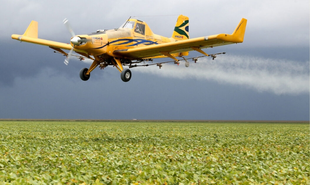 Avião agrícola pulveriza pesticidas sobre plantação, prática associada à deriva de agrotóxicos em terras indígenas.