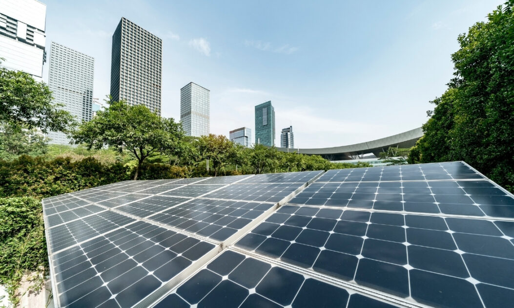 Painéis solares instalados em área urbana com cidade ao fundo, representando a expansão da transição energética e suas desigualdades globais
