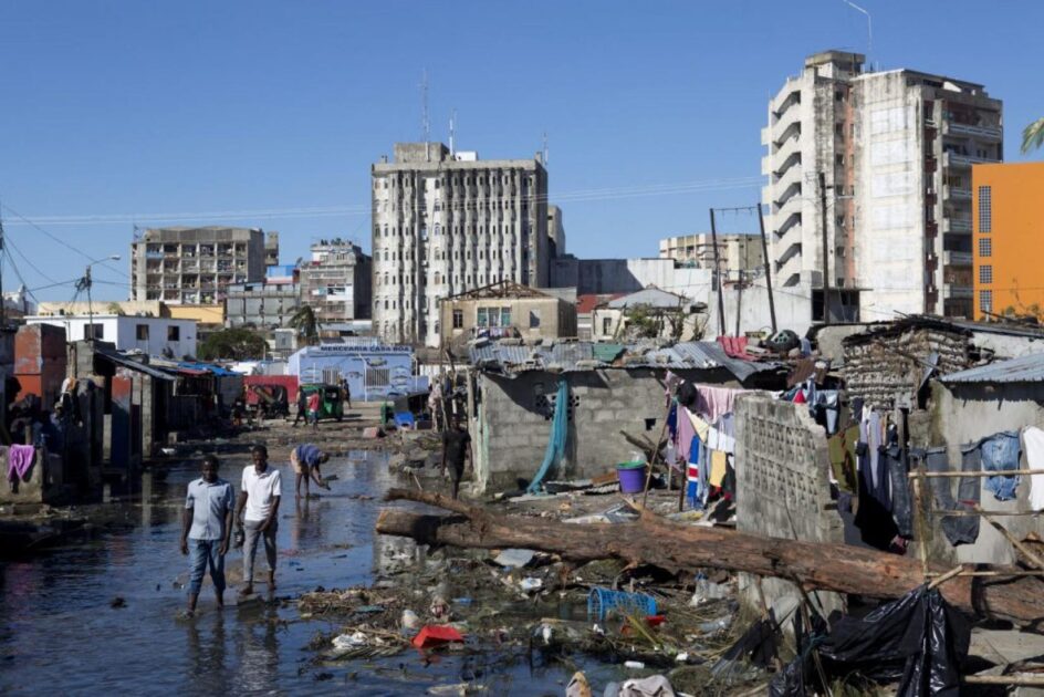 Moradores caminham por área alagada em Beira, Moçambique, após ciclone Idai, exemplo de desastres naturais com impacto social e eleitoral.
