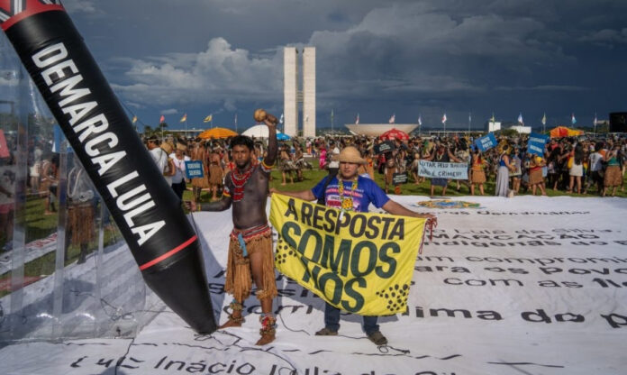 Manifestação indígena em Brasília durante o Acampamento Terra Livre com faixa e símbolo contra exploração, defendendo zonas livres de petróleo e gás