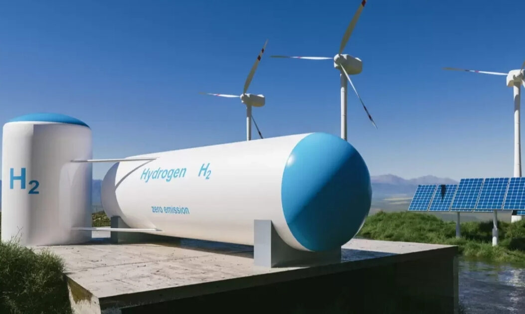 Carro movido a hidrogênio mira recorde mundial de velocidade e emissão zero 1 Tanques de hidrogênio com indicação H₂ em área de energia renovável, com placas solares e aerogeradores ao fundo, representando o uso de hidrogênio verde.